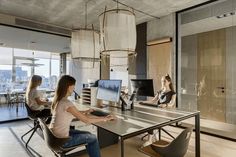 three women are sitting at a table in an office setting with computers on the desk