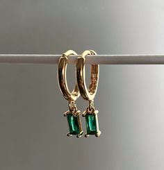 Dainty gold huggies perfect for everyday wear.  Details: - 18k gold plated hoop earrings. - Cubic zirconia emerald pendants. - Clicker hoop closure. - Comes in a beautiful silk pouch. Dimensions: - Hoop: 17x13.5x2mm. - Pendant: 8.5x4x3mm. Shipping: - FREE UK DELIVERY, next day dispatch. - Royal Mail 2nd class. Upgrade to UK Express Shipping: - £1 for Royal Mail 1st class, next day dispatch. Thank you for checking out my store <3. Luxury Green Huggie Earrings Fine Jewelry, Luxury Yellow Gold Hoop Earrings With Emerald, Dainty Green Huggie Earrings As Gift, Green Tarnish Resistant Huggie Earrings For Gifts, May Birthstone Huggie Earrings Gift, May Birthstone Small Hoop Huggie Earrings Gift, Gift May Birthstone Drop Earrings, Gold Huggie Earrings For May Birthstone Gift, Small Gold Hoops