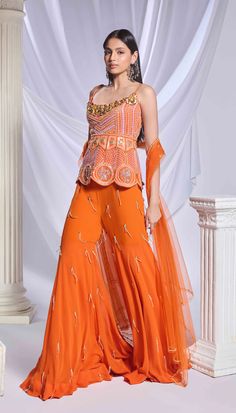 Our burnt orange 3-piece sharara set comprises of a peplum top, sharara, and dupatta. The peplum top is adorned with delicate embroidery featuring crystals, pearls, and sequins, alongside gold metallic flowers embellishing the front neckline and scalloped hem. The georgette sharara is bejewelled with crystal tassels. Completing the ensemble is a matching dupatta, embellished with scatter embroidery and finished with a delicate pearl and golden border.From Papa Don’t Preach’s Bring Your Own Fairy Orange Sharara, Punjabi Sharara Suits, Metallic Flowers, Pink Sharara, Georgette Sharara, Golden Border, Delicate Embroidery, Sharara Set, Orange Fabric