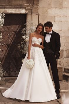 a bride and groom standing in front of an arch with white flowers on the side