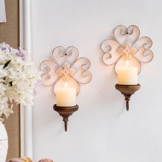 two wall sconces with candles in them on the wall next to a vase filled with flowers