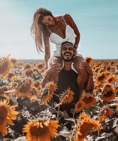 a man holding a woman on his back in a field of sunflowers