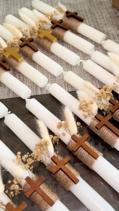 many candles are lined up with crosses and feathers on them, along with some dried flowers