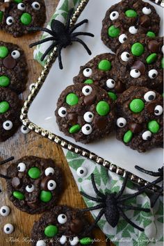 chocolate cookies decorated with green eyes and spider webs on a white plate next to other cookies