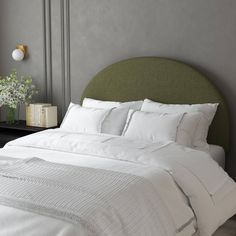 a bed with white linens and pillows in a gray room next to a lamp