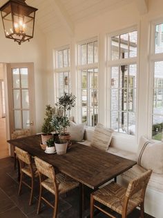 a dining room table with chairs and a bench in front of large windows that look out onto the yard