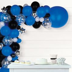 a table topped with balloons and cake next to a white wall covered in black and blue decorations