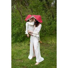 two people dressed in white with red umbrellas and one holding a baby on her back