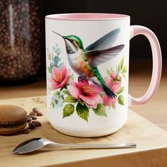 a hummingbird painted on a coffee mug next to a spoon and cup with beans