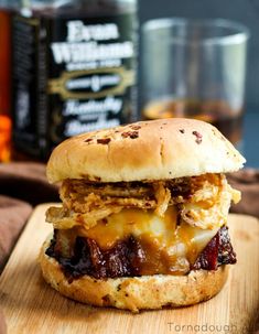 a sandwich with meat and cheese sitting on top of a cutting board next to a bottle of whiskey