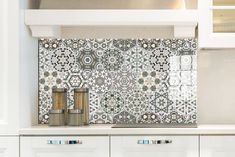 a kitchen with white cabinets and an intricate tile backsplash in the center, along with two salt shakers