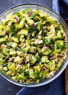 a glass bowl filled with chopped vegetables on top of a blue cloth next to a wooden spoon