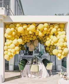 an outdoor dining area with yellow balloons hanging from the ceiling and green chairs around it