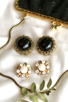 large, gold clip on earrings with round black stone and flower shaped clip on earrings with a pearl center placed next to black vintage kisslock purse. Earings Aesthetics, Ear Rings Gold, 50s Earrings, Diana Earrings, School Earrings, Vintage Earrings Gold, 60s Earrings, 70s Earrings