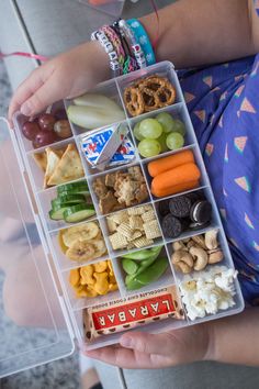 a child holding a plastic container filled with different types of food and snacks in it