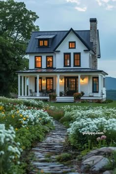 a white house with lots of windows and flowers in the front yard, along with a stone path leading up to it