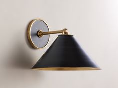 a black and gold wall light with a white shade on the side, against a white wall