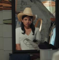 a woman wearing a cowboy hat standing in front of a mirror