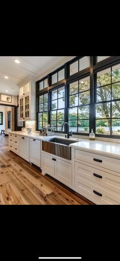 a large kitchen with white cabinets and wood flooring is pictured in this image, there are windows that look out onto the water