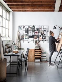 a woman standing in front of a easel with pictures on the wall