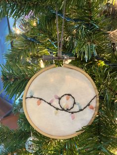 a hand embroidered ornament hanging from a christmas tree with pine needles and lights