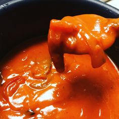 an orange sauce in a black bowl with a wooden spoon sticking out of the top