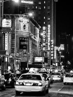 black and white photograph of traffic in new york city at night with neon signs on buildings