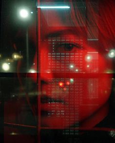 a woman's face is reflected in a window with red light shining through it