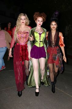 three women dressed in costume walking down the street at night with other people behind them