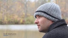 a man wearing a knitted hat looks out over a body of water with trees in the background