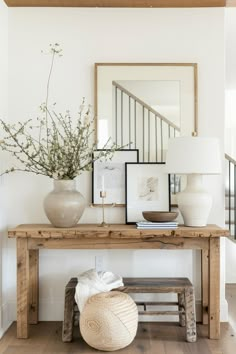 a wooden table topped with a vase filled with flowers next to a mirror and lamp