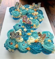 cupcakes with blue frosting are arranged on a white platter in front of a wooden table