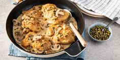 a skillet filled with chicken and mushrooms next to a bowl of olives on the side