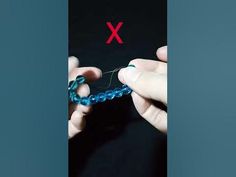 two hands are knitting beads together on a black surface with red x in the background