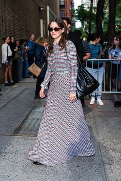 a woman in a long dress is walking down the street with her hand on her hip