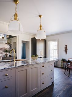 a large kitchen with marble counter tops and gold accents on the lights over the island