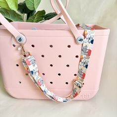 a pink purse with flowers on it sitting next to a potted plant