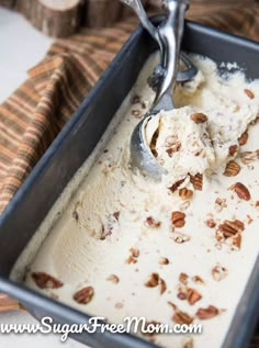 a scoop of ice cream in a pan with pecans on the side and a spoon sticking out