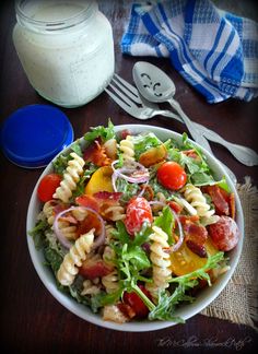 a salad with bacon, tomatoes, lettuce and other toppings in a white bowl