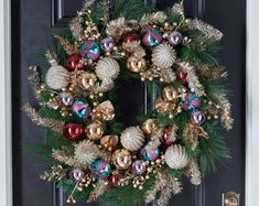 a christmas wreath on the front door with ornaments hanging from it's sides and pine cones