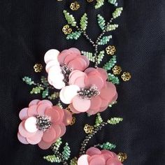 three pink flowers with green leaves on a black background, surrounded by beads and sequins