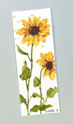 a watercolor painting of two sunflowers on a white card with green leaves