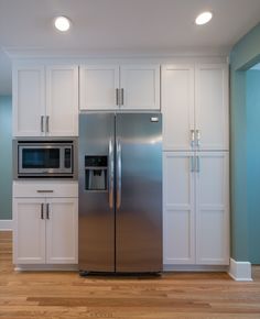 a silver refrigerator freezer sitting inside of a kitchen next to white cabinets and drawers