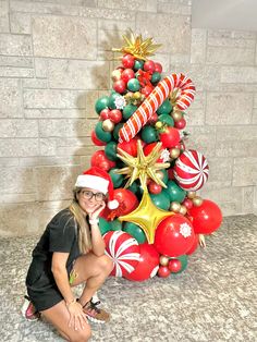 a woman kneeling next to a christmas tree with balloons and candy canes on it