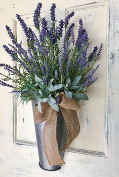 a metal vase filled with purple flowers on top of a wooden door sill next to a burlap bow