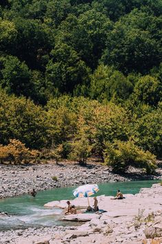 people are sitting on rocks in the middle of a river with an umbrella over them