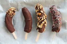 four chocolate covered donuts with sprinkles and nuts on them are lined up in a row