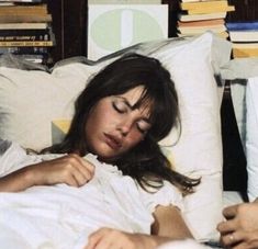 a woman laying in bed with her eyes closed and hands on the pillow as she sleeps