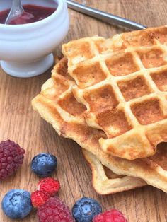 three waffles with raspberries and blueberries next to syrup on a table