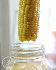 corn on the cob in a mason jar with liquid pouring from it to its ear